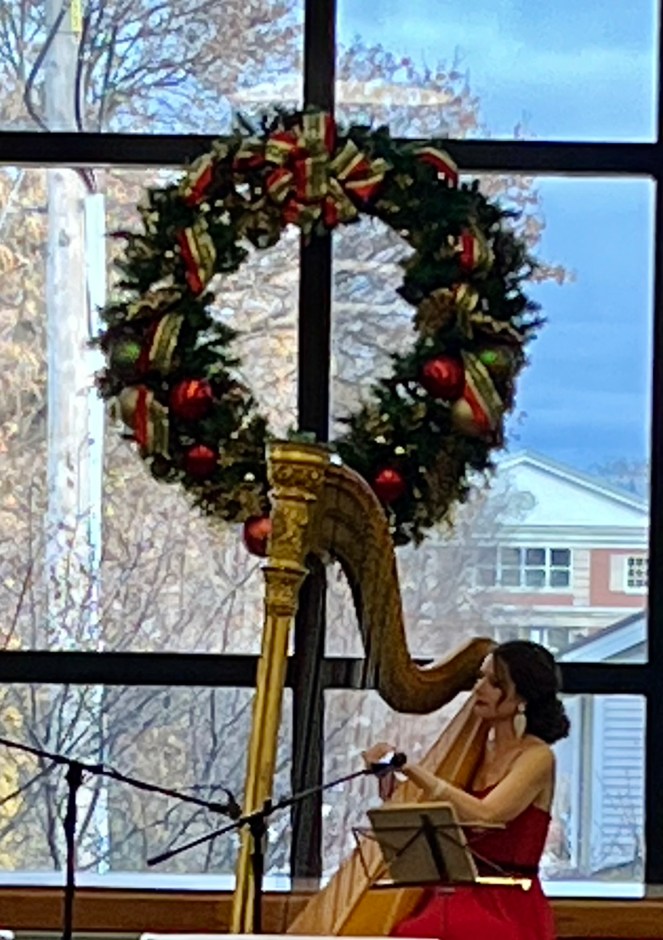 Harpist in in front of a large window with a wreath on it playing a standing harp. Winter, Glen Ellyn, 2024